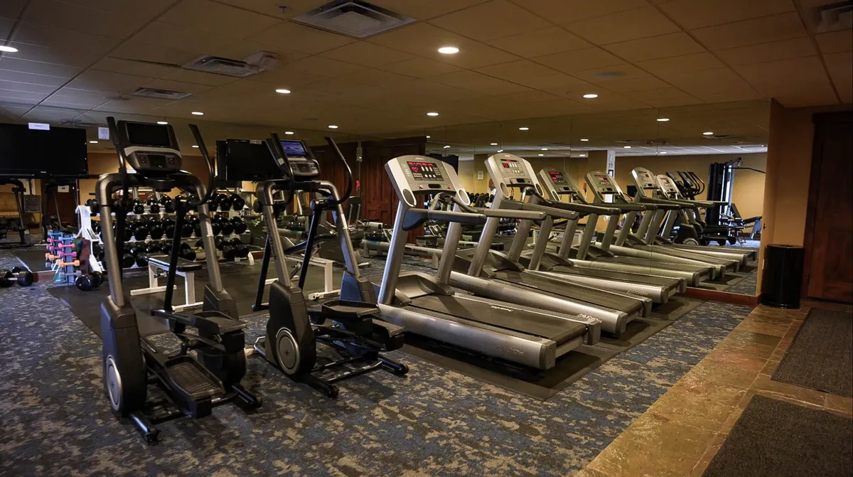 A well-lit, modern fitness center interior featuring treadmills, elliptical machines, and a dumbbell rack. The space is bright and active, inviting guests to pursue their wellness routines in style.