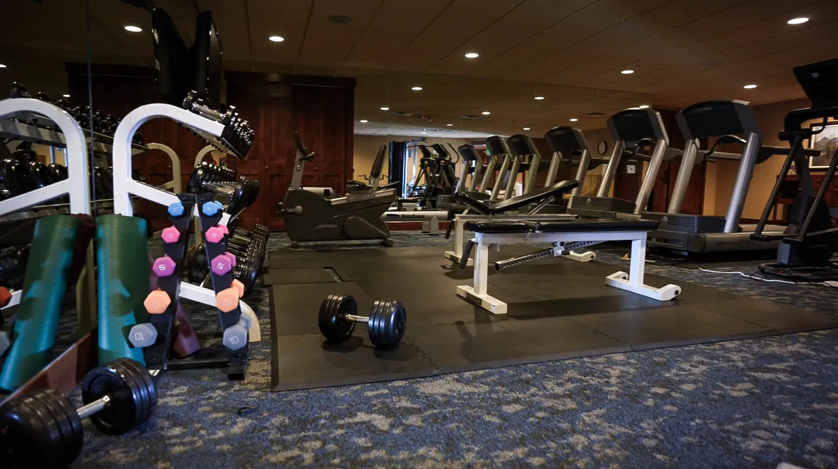 This image showcases a vibrant fitness center with dumbbells, treadmills, exercise benches, and mats. The scene is lively and motivating, with ample space for group workouts and personal fitness routines, reflecting a shared environment where guests can pursue their health goals.