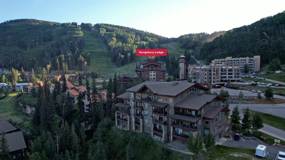 This image showcases the exterior of Purgatory Lodge, with the stunning Needles Range mountains in the background and a tree line framing the scene. There's a sense of serenity and adventure, with hints of activities like skiing, hiking, and evening gatherings visible through the lodge's vantage point and outdoor spaces.