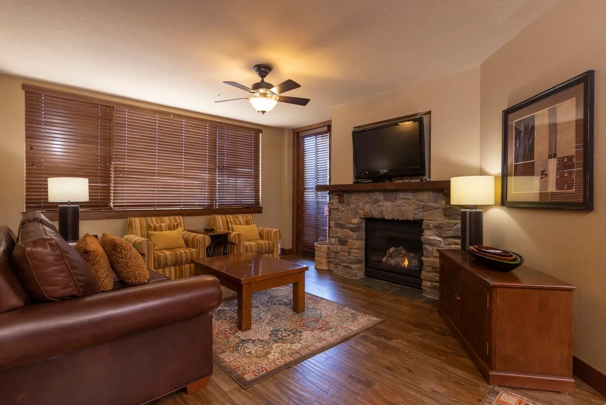 The image showcases a warm, inviting living area featuring a cozy fireplace, plush sofa, and large windows that frame scenic mountain views. The space is perfect for unwinding after a day on the slopes, gathering for games, or sipping hot cocoa by the fire.