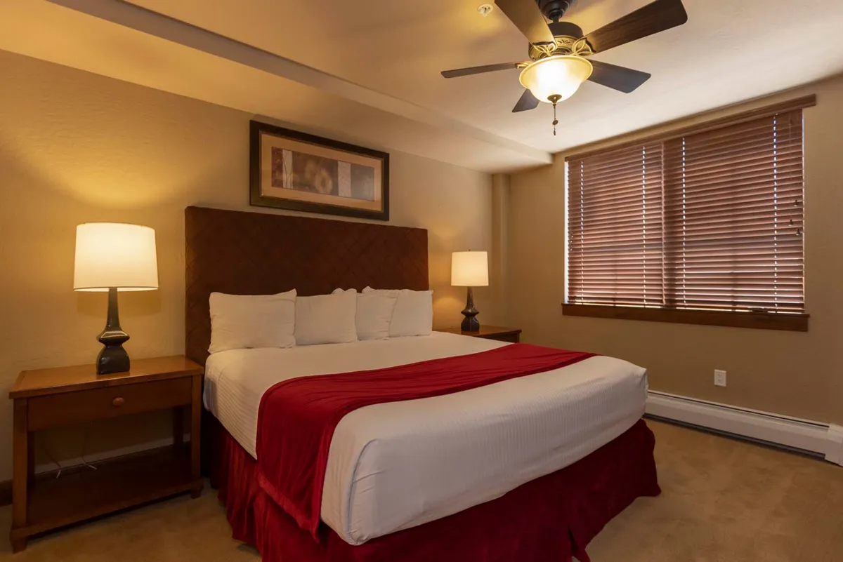 A second inviting bedroom scene with a king-sized bed, crisp white linens, nightstands with lamps, and elegant wall art. The mood is cozy and comfortable, suggesting a space designed for rejuvenation and peaceful sleep.