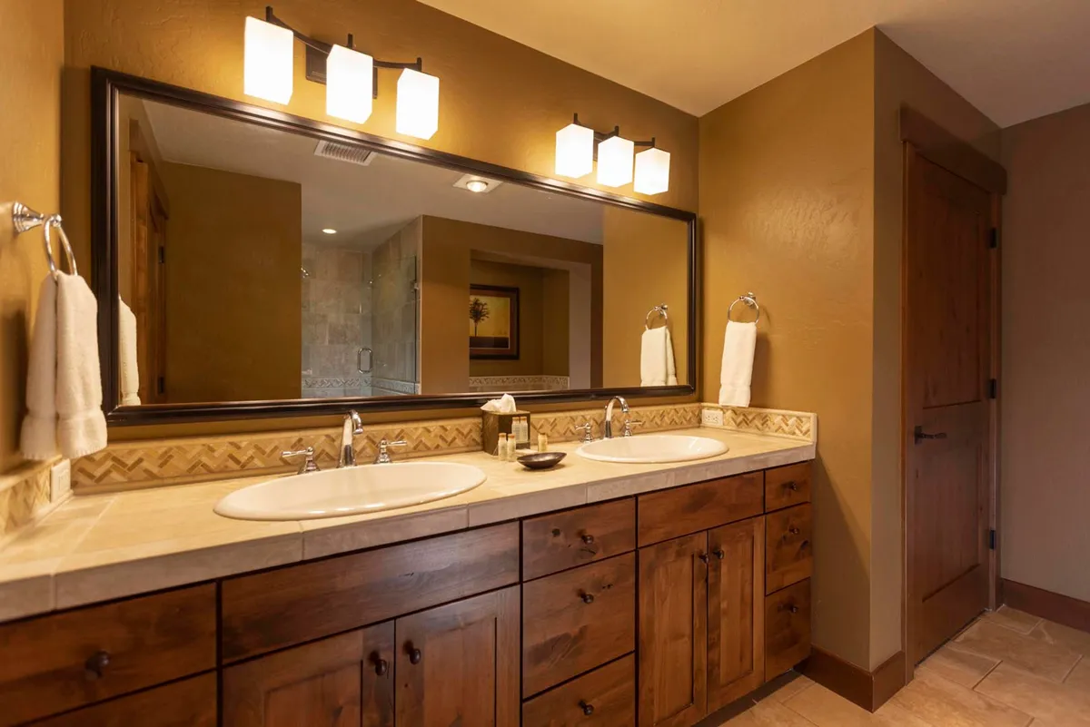 A serene bathroom featuring a double sink vanity, a large mirror, and stylish decorative lighting. The calm, uncluttered space invites indulgence in morning and evening routines, hinting at luxurious finishes and privacy.