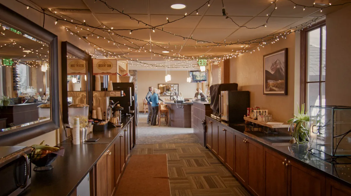 A warm and inviting barista station and seating area, accentuated by decorative lighting. The image captures a friendly, social environment perfect for gathering with friends, sharing stories, and unwinding after a day of adventure.