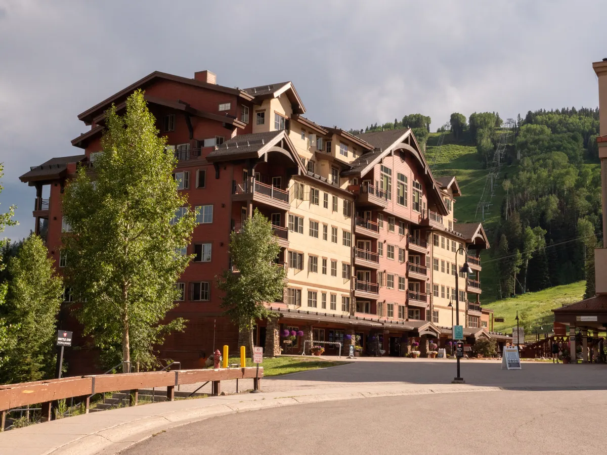 A welcoming view of the lodge’s architecture set against the backdrop of ski slopes and towering trees. Outdoor seating hints at social gatherings, and the surrounding environment connects guests to mountain exploration and local dining.