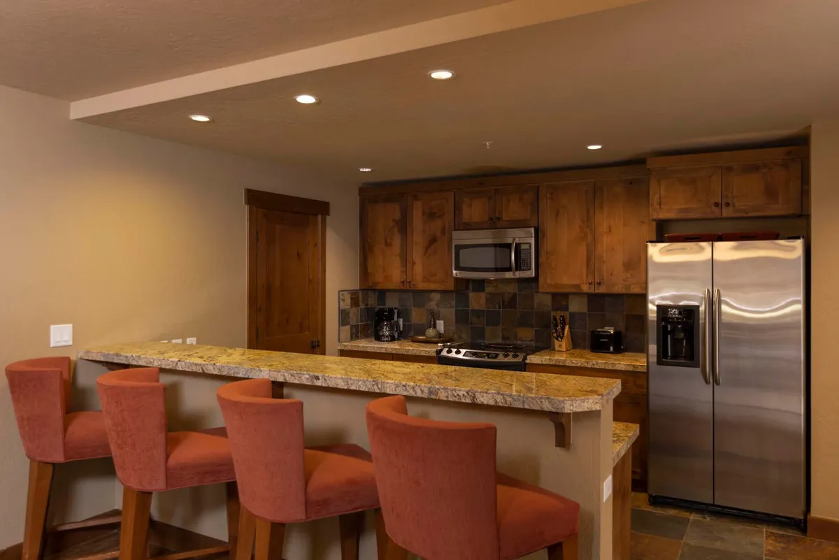A spacious alpine kitchen featuring gleaming granite countertops, stainless steel appliances, warm wooden cabinets, and bar stools. The open layout allows for easy interaction with guests, while the inviting atmosphere is perfect for cooking or entertaining.